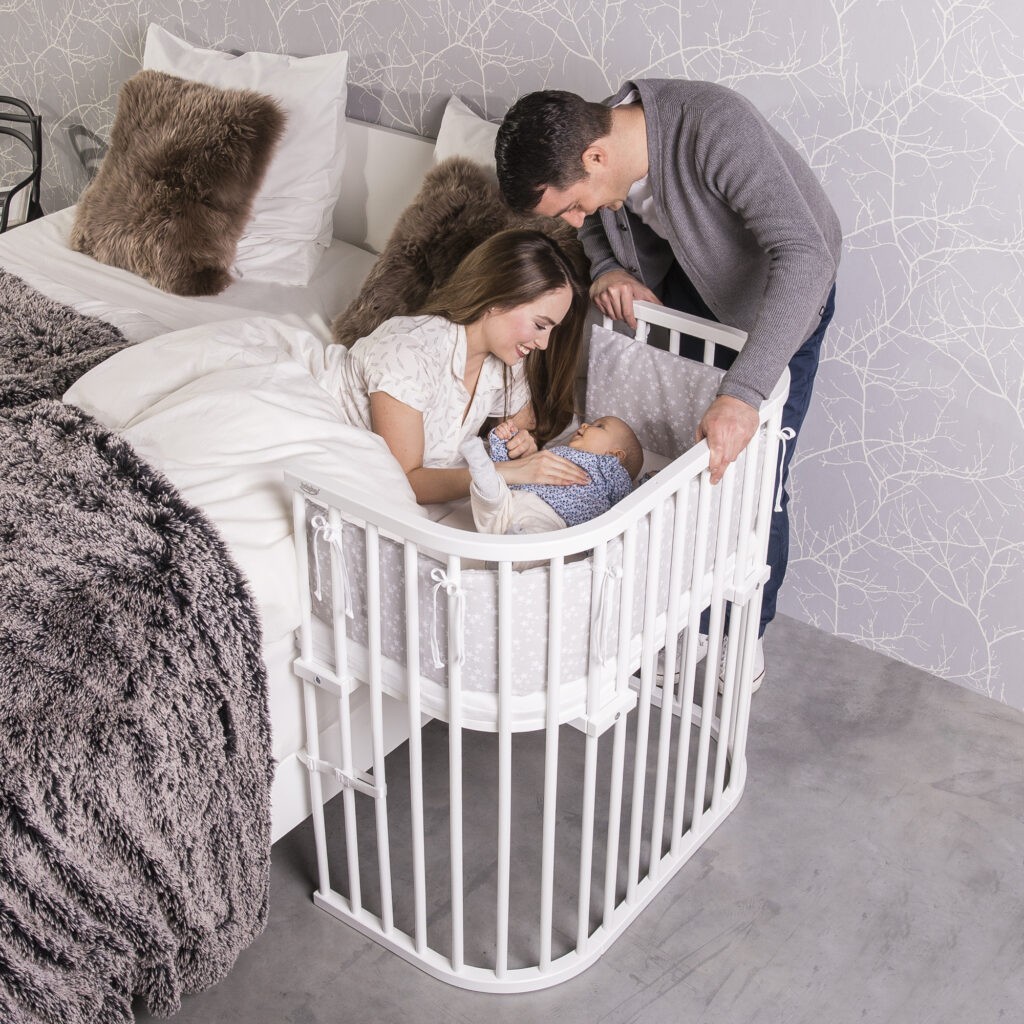 Eltern beugen sich über ihr Baby im babybay® Boxspring Beistellbett