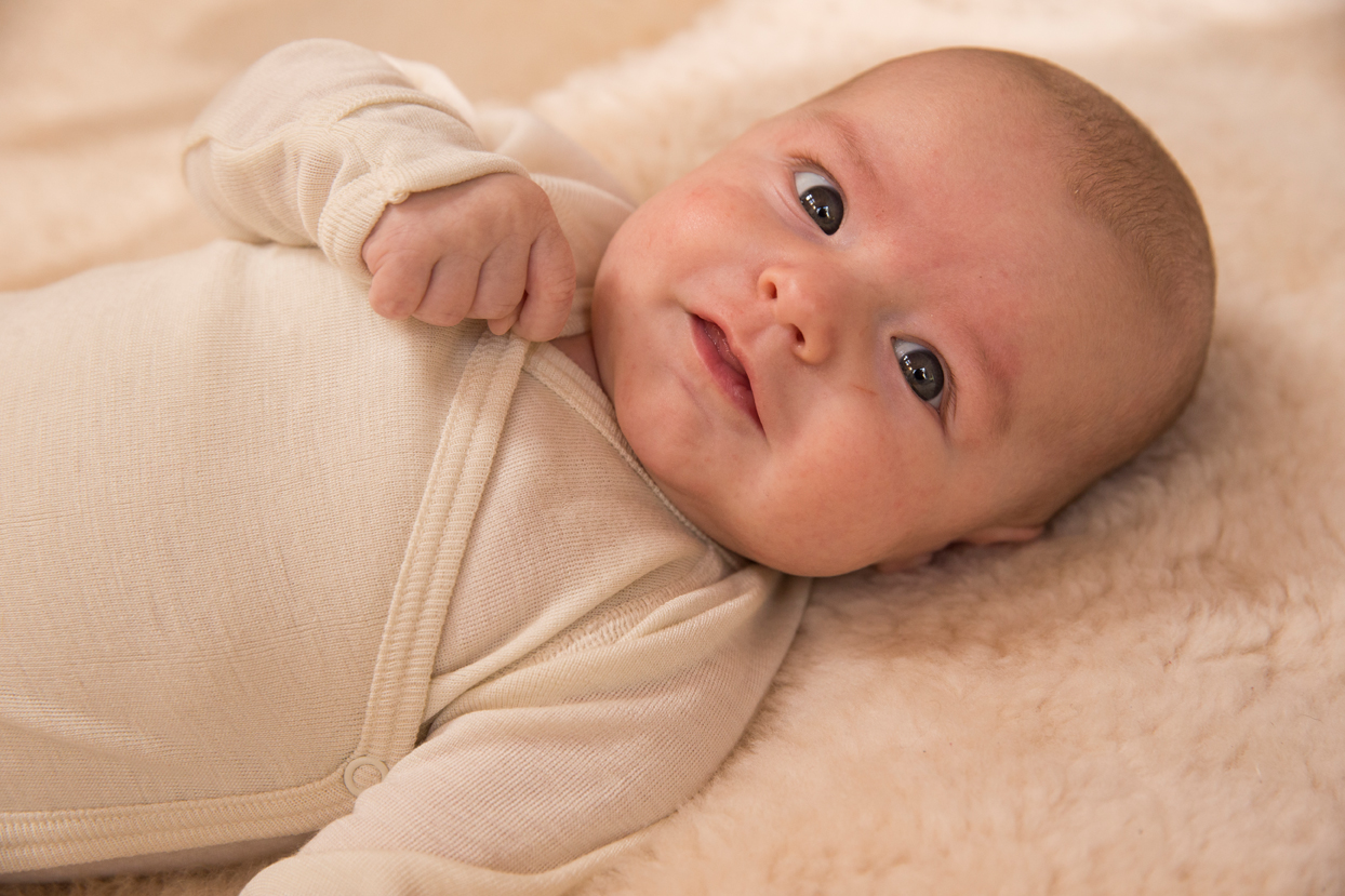 Baby im hessnatur Langarm-Wickelbody liegt auf dem Rücken auf einem Teppich