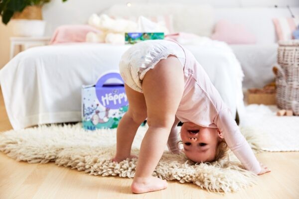 Kleinkind macht Kopfstand im Hintergrund sieht man eine Packung bella baby Happy Windeln