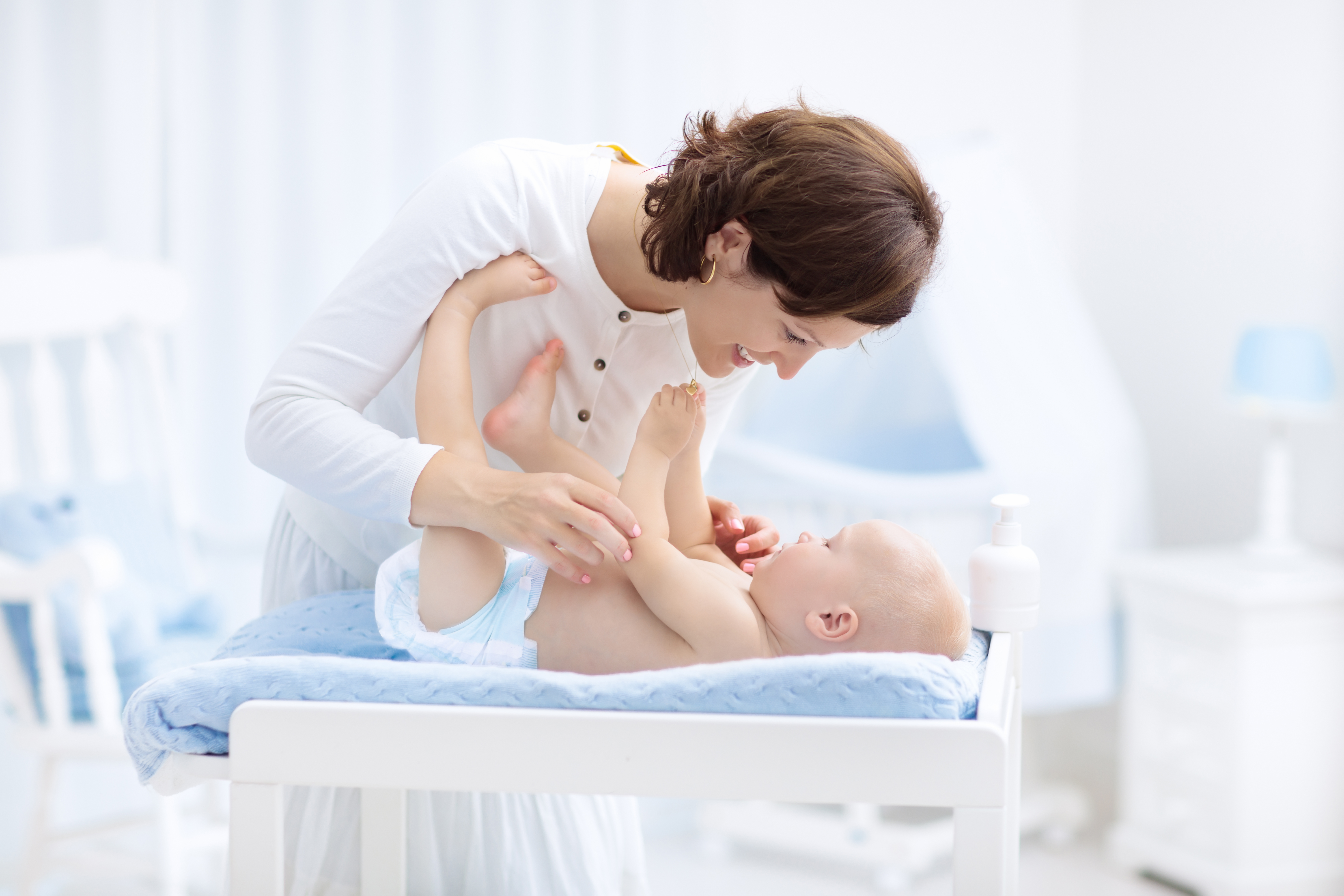 Mutter spielt mit ihrem Baby auf Wickeltisch, welches die ROSSMANN Babydream Windeln trägt